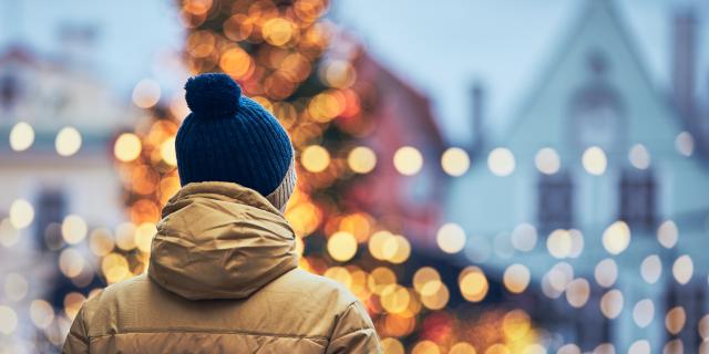 Rear view of man in warm clothing during walk in city. Christmas tree and decoration in Old Town in Tallinn, Estonia.