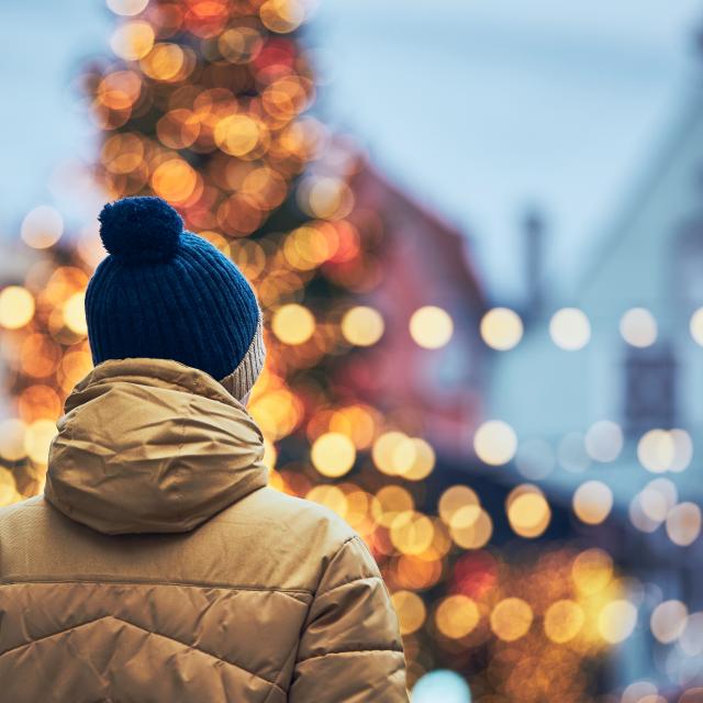 Rear view of man in warm clothing during walk in city. Christmas tree and decoration in Old Town in Tallinn, Estonia.