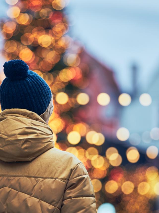 Rear view of man in warm clothing during walk in city. Christmas tree and decoration in Old Town in Tallinn, Estonia.