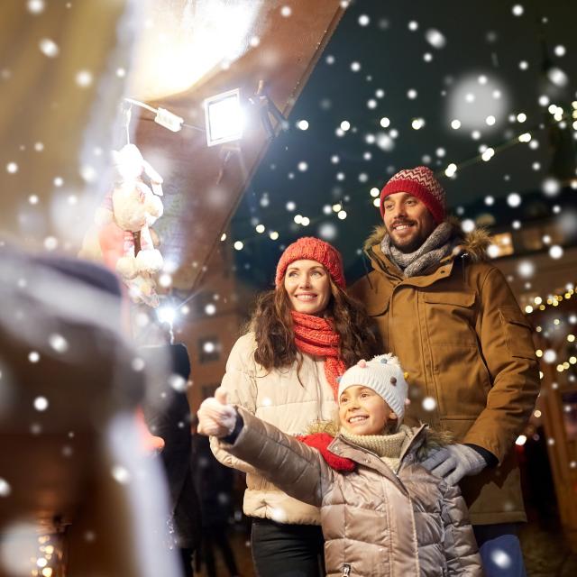 family, winter holidays and celebration concept - happy mother, father and little daughter at christmas market on town hall square in tallinn, estonia over snow