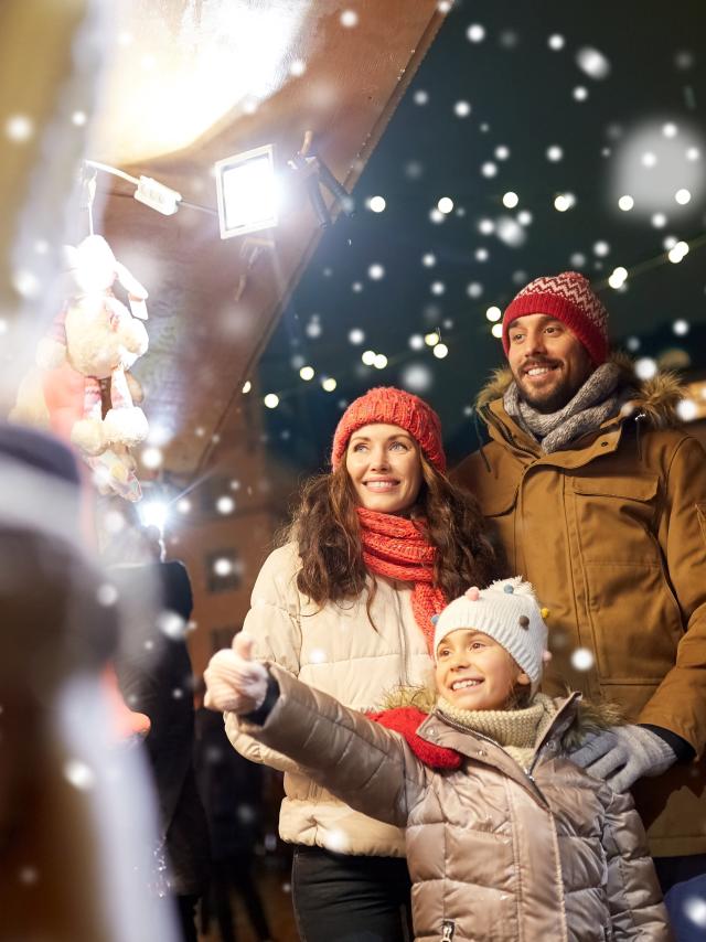 family, winter holidays and celebration concept - happy mother, father and little daughter at christmas market on town hall square in tallinn, estonia over snow